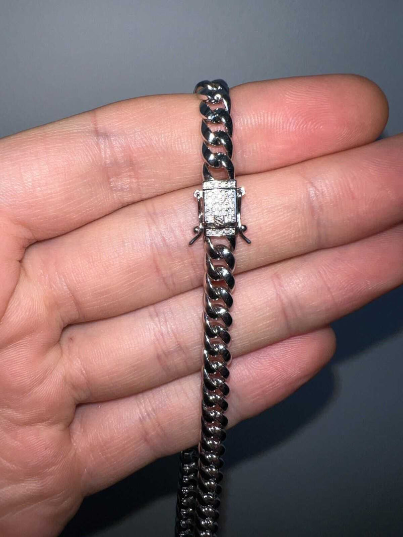 Men's moissanite Cuban curb link chain in solid 925 silver with rhodium finish, held in a hand.
