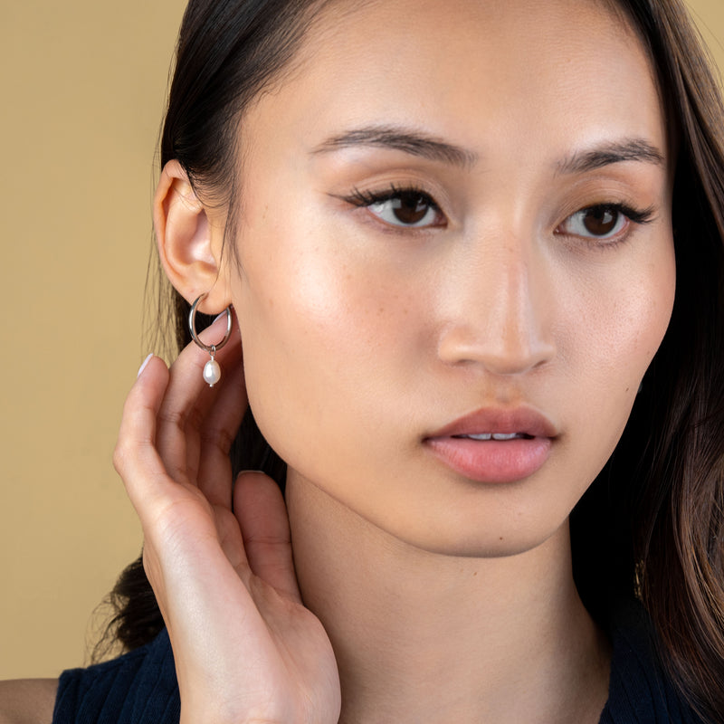 Gold pearl huggie hoops with natural freshwater pearl charm worn by a model.