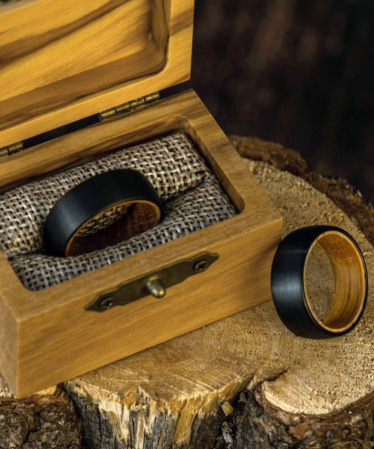 Black satin tungsten ring with etched outer and olive wood inner bands in a wooden box.