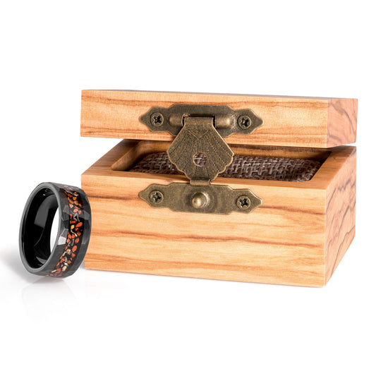 Black tungsten ring with dinosaur bone and meteorite inlay next to a wooden box.